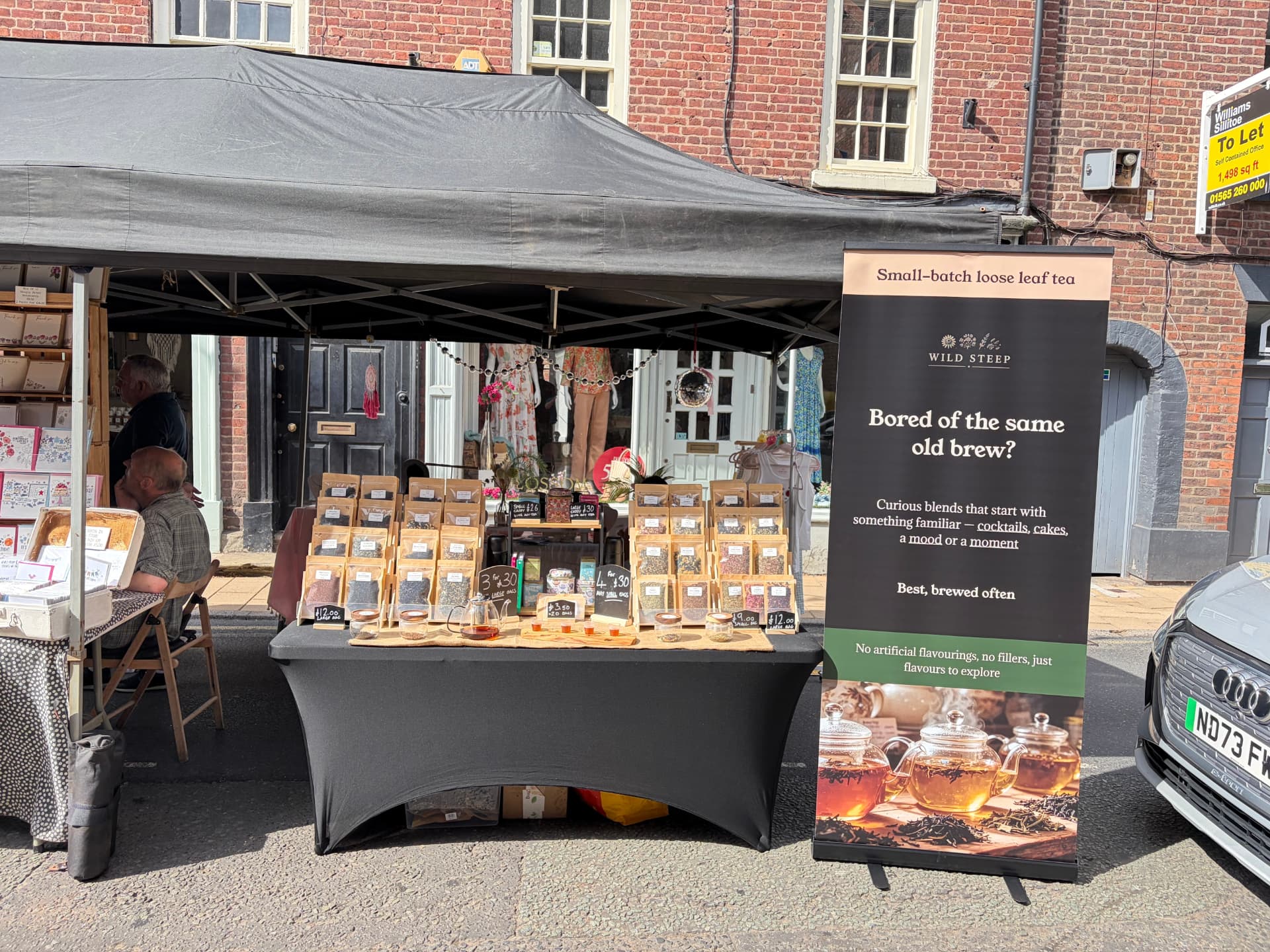 Wild Steep market stall — brass scales, wicker baskets of loose leaf tea and apothecary jars of botanicals at an outdoor craft market